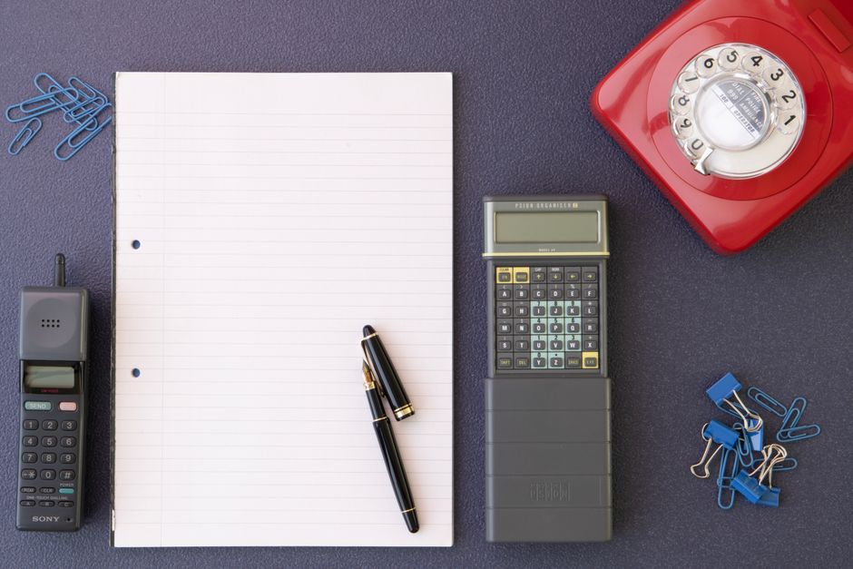 Flat lay of vintage office setup featuring a rotary phone, calculator, and stationery.